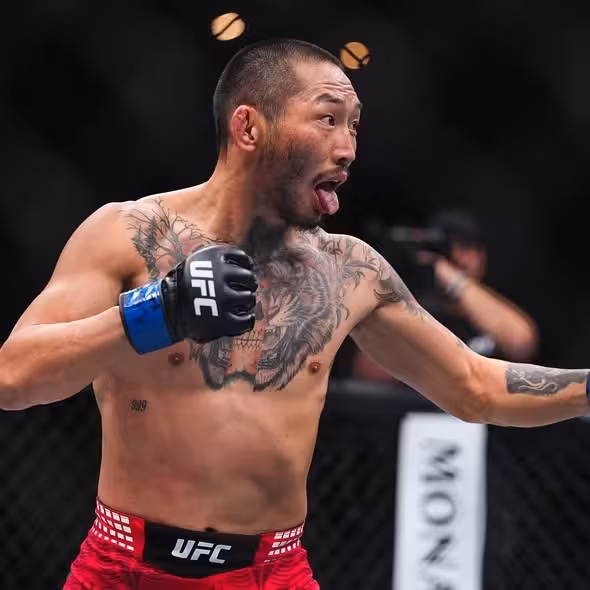 UFC flyweight Nyamjargal Tumendemberel sporting a prominent tiger chest tattoo and red trunks reacts intensely during his fight at UFC 326